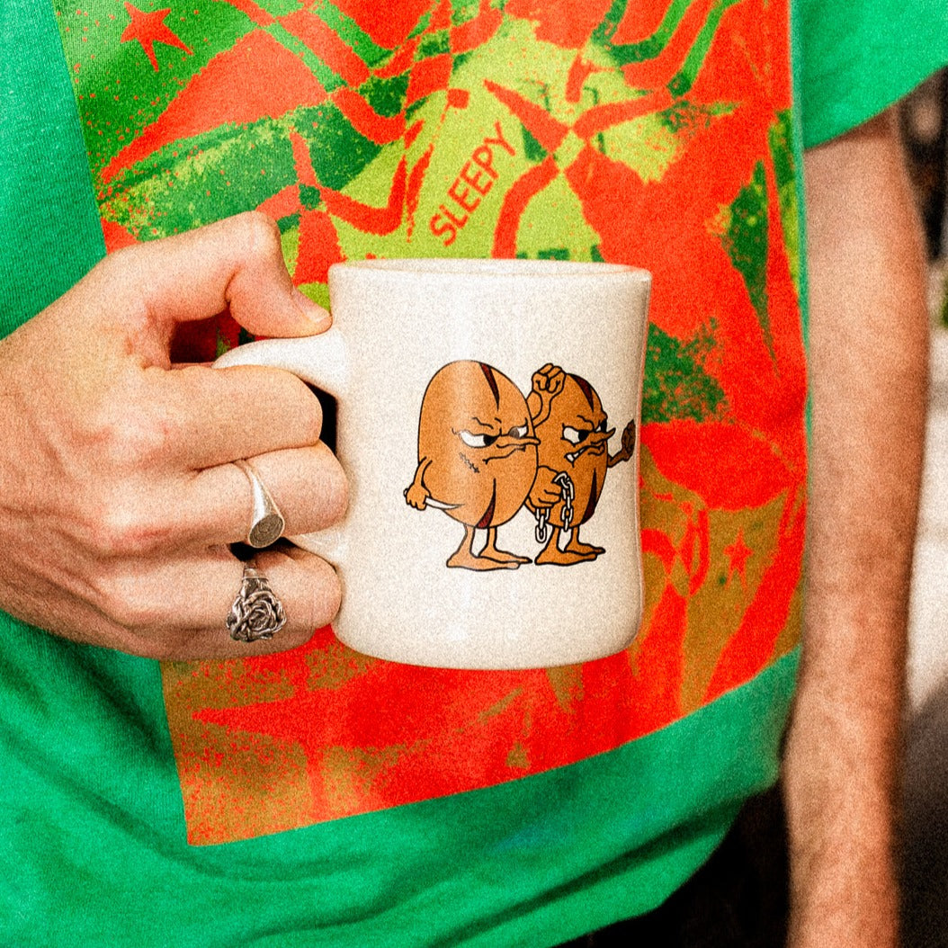 man holding grouch and co mug with two agressive coffee beans who are threatening to 'Mug' you. 