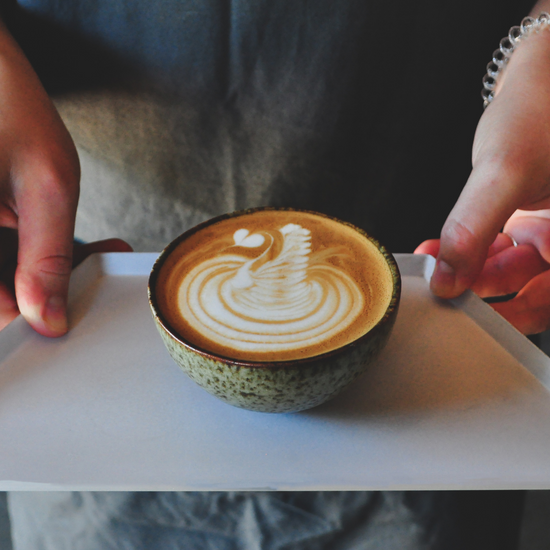 Hand made ceramic coffee cup on a pink tray with a swan design in latte art